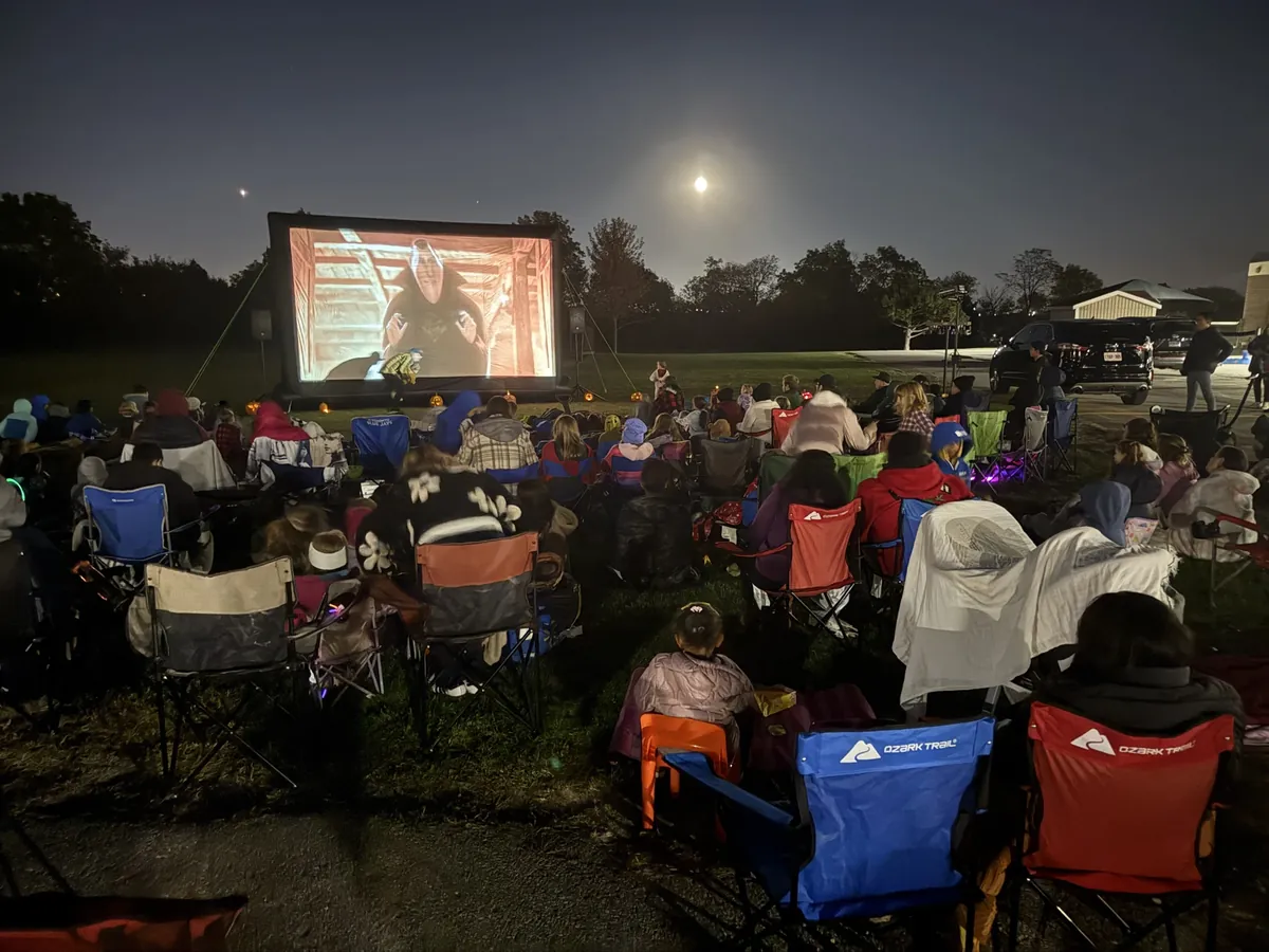 Families seated outdoors watching a movie on a large inflatable screen